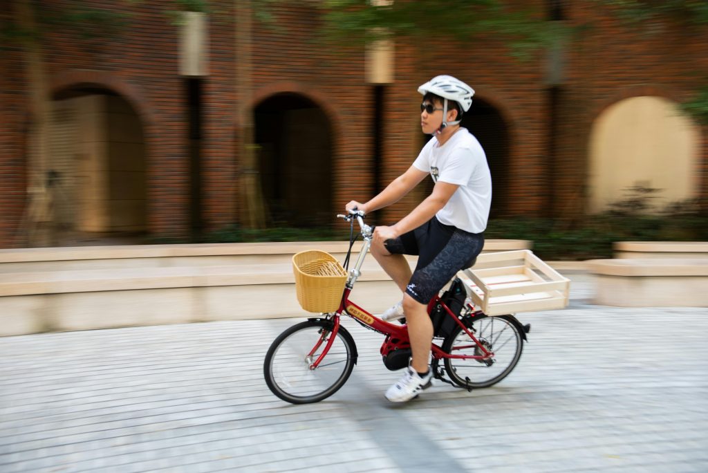 Man wearing a helmet rides a red bike with a basket in an urban area.