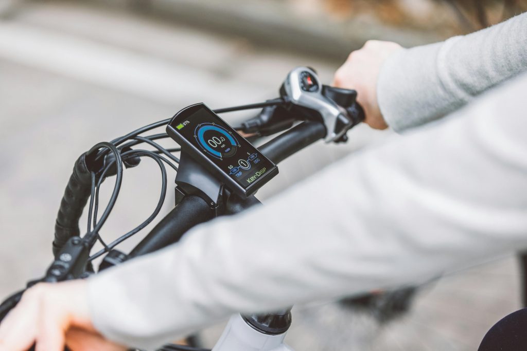 Hands gripping the handlebar of an electric bicycle, showcasing the digital display screen for speed and battery status.