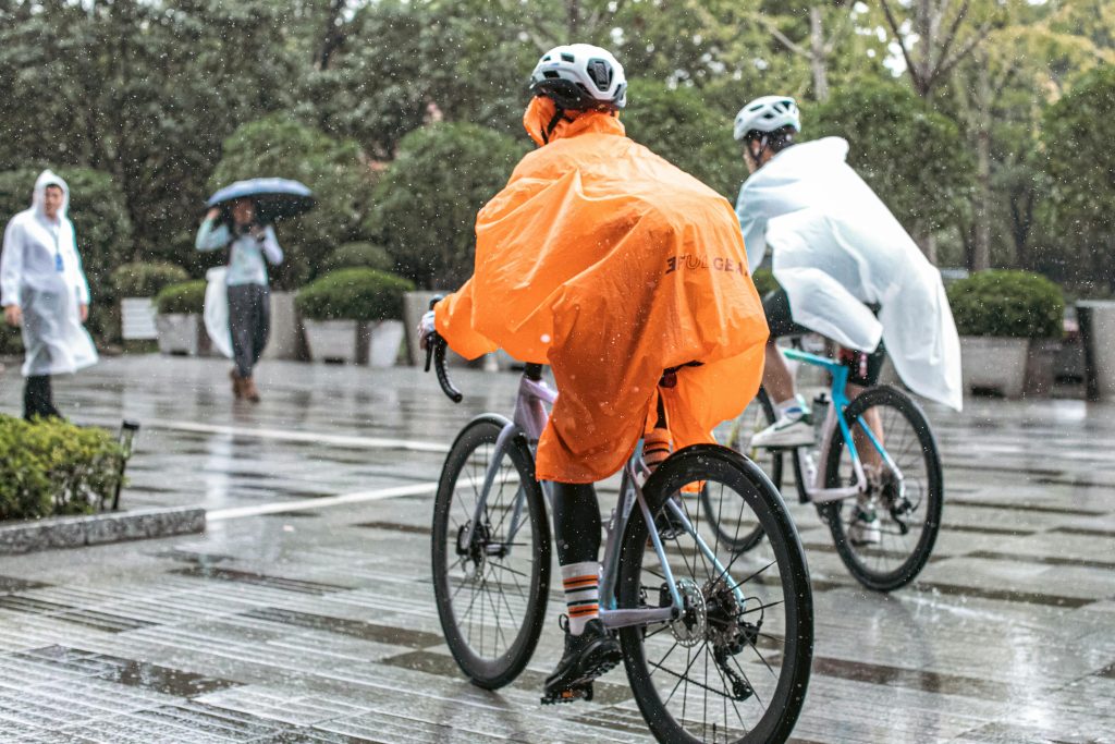 Cyclists wearing rain ponchos ride in the rain on a paved path, showcasing resilience.