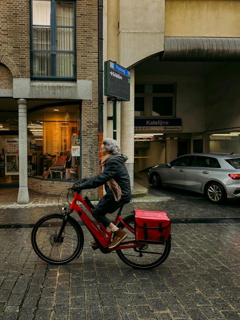 A senior woman riding a bicycle on a cobblestone street in Bruges, Belgium.