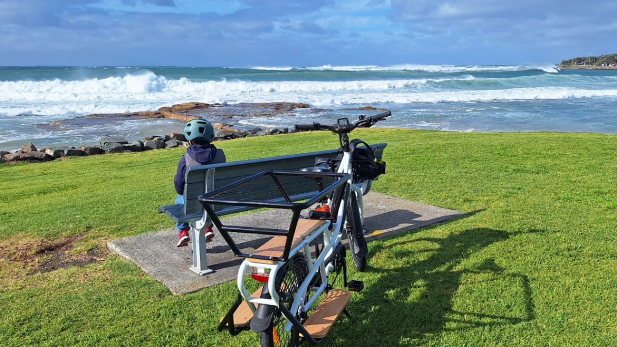 Child wearing a helmet beside a cargo ebike overlooking the Wollongong coastline