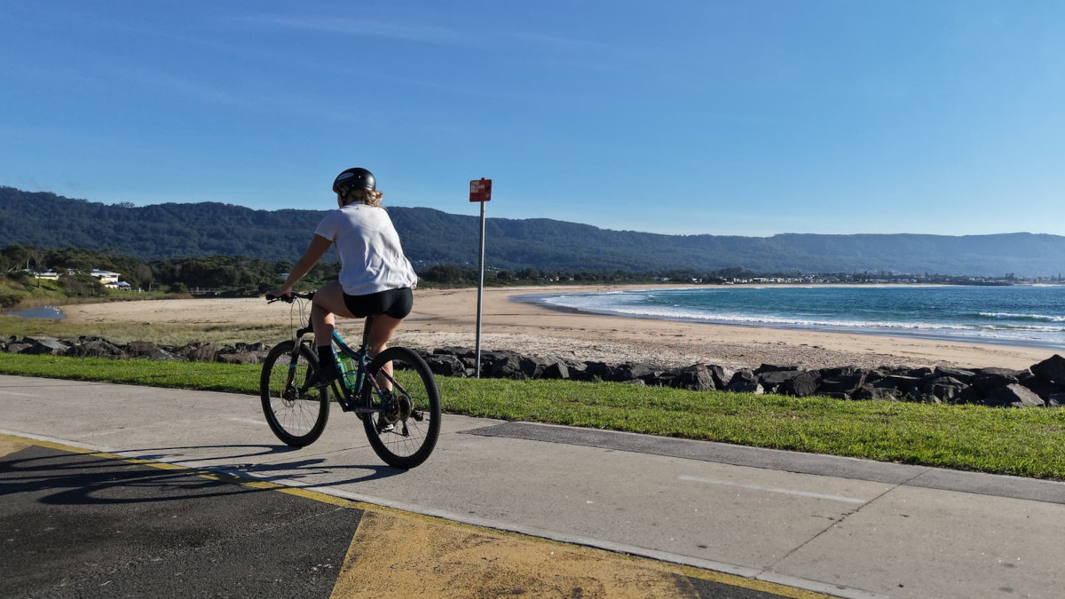 Cyclist riding the shared coastal path between Thirroul and Wollongong with ocean and escarpment views.