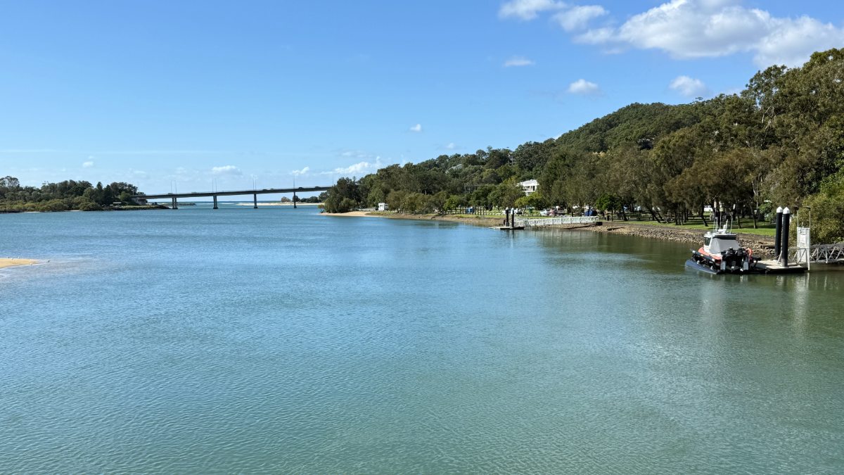Calm waters of Currumbin Creek with parkland and bridge in the distance